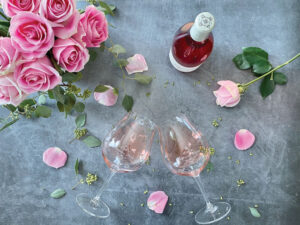 Roses, glasses of Rosé and a bottle of Domaine Divio Rosé on a grey table.