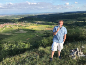 Domaine Divio winemaker, Bruno Corneaux, sipping wine on a hillside in France.